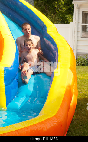 family water slide in back yard at home with water in summer with dad playing with boy riding age 10 Stock Photo