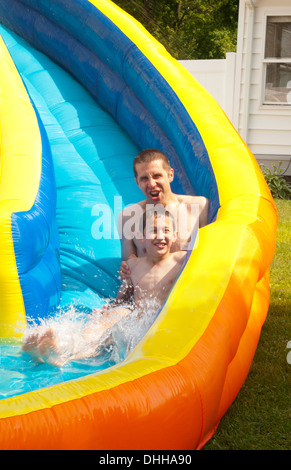 family water slide in back yard at home with water in summer with dad playing with boy riding age 10 Stock Photo