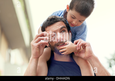Father carrying son on shoulders, boy covering man's eye Stock Photo