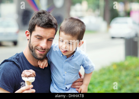 Father holding ice cream, son licking lips Stock Photo