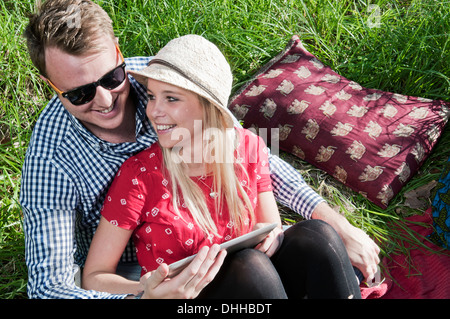 Young couple sitting on picnic blanket using digital tablet Stock Photo