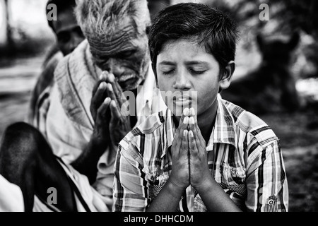 Indian boy in prayer whilst waiting at Sri Sathya Sai Baba mobile outreach hospital. Andhra Pradesh, India. Monochrome Stock Photo