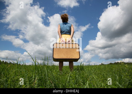 Teenage girl holding suitcase in field Stock Photo