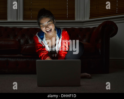 Young woman sitting on floor laughing at digital tablet Stock Photo