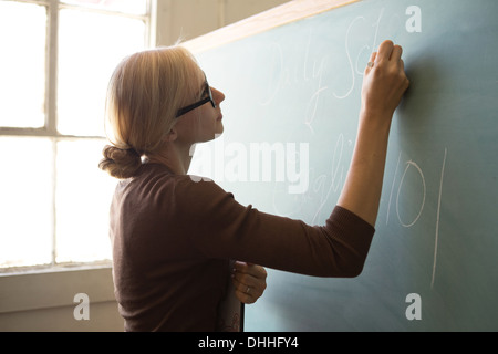 Teacher writing on blackboard with chalk Stock Photo