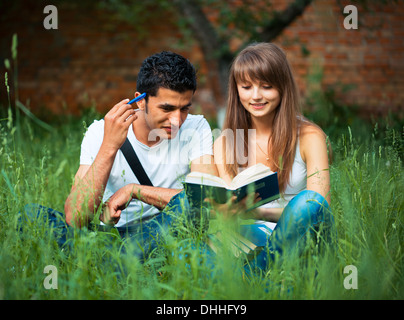 Two students guy and girl studying in park on grass with book outdoors Stock Photo