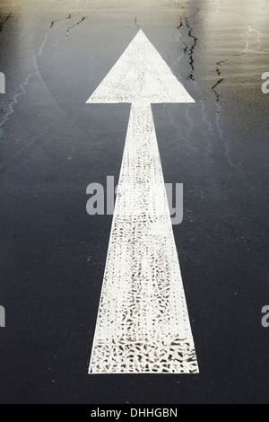 white painted road arrow marking on a black road surface Stock Photo