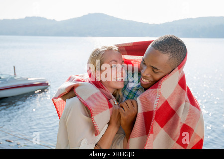 Young couple wrapped in blanket by lake, Hadley, New York, USA Stock Photo