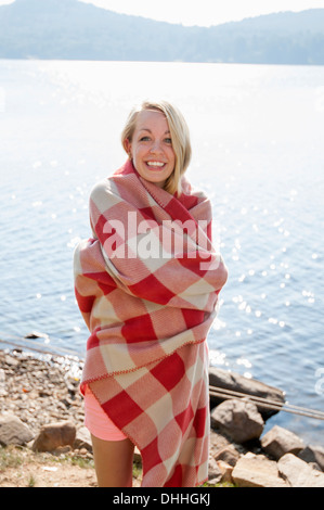 Young woman wrapped in blanket by lake, Hadley, New York, USA