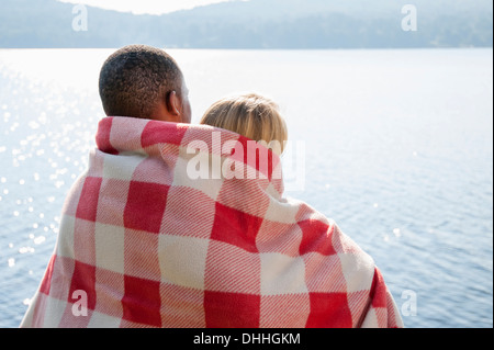 Young couple wrapped in blanket by lake, Hadley, New York, USA