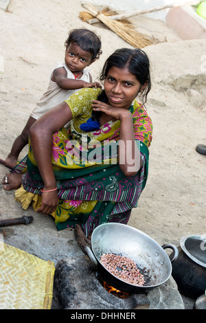 Indian teenage girl and child cooking peanuts on an open fire outside her home in a rural village. Andhra Pradesh, India Stock Photo