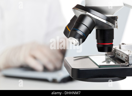 Researcher working on laptop behind microscope Stock Photo