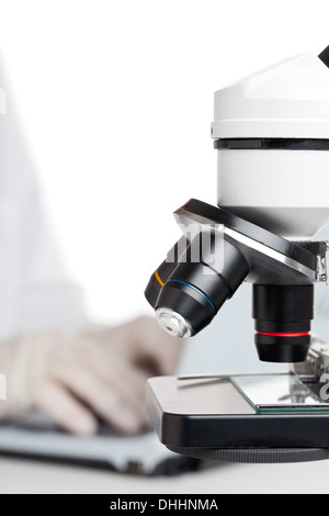 Researcher working on laptop behind microscope Stock Photo