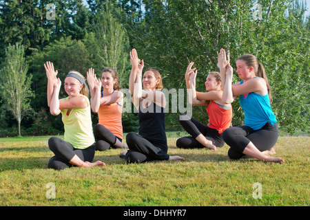 Teenage girls and tutor sitting on grass doing yoga Stock Photo
