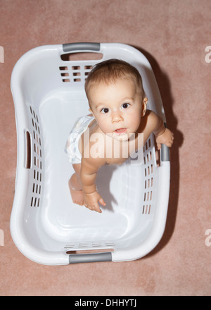 Baby girl standing in laundry basket, high angle