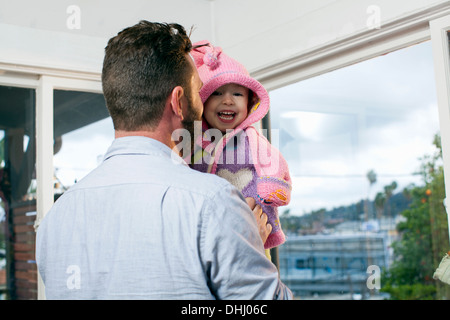 Father dressing daughter in hooded knitted top Stock Photo