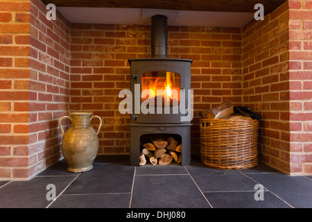 Fire in wood burning stove in brick fireplace with basket of cut wood ready for burning Stock Photo