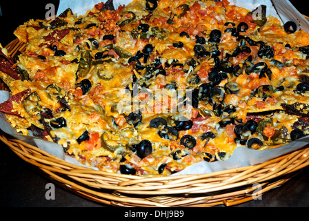 Huge wicker basket platter nachos pub fast food red yellow corn tortilla chips cheese sliced olives peppers tomatos Stock Photo
