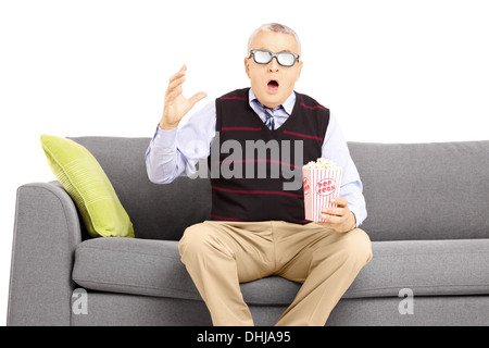 Shocked senior man with popcorn box sitting on a sofa and watching movie Stock Photo