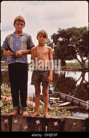 This photograph features boys with an airgun and a bird, living in the wetlands of Bayou Gauche, Louisiana. The image reflects the rural lifestyle of fishing families in the region. Stock Photo