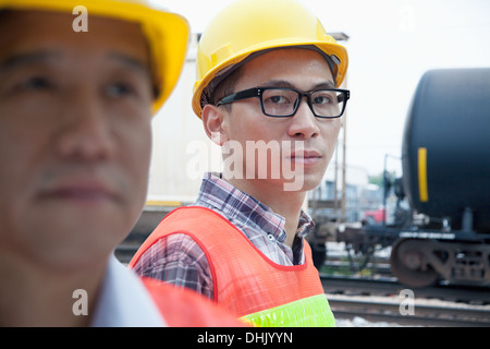 Serious engineer in protective workwear looking at camera outside in front of railroad tracks Stock Photo