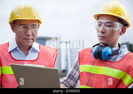 Two engineers in protective workwear looking down at a clipboard outside of a factory Stock Photo