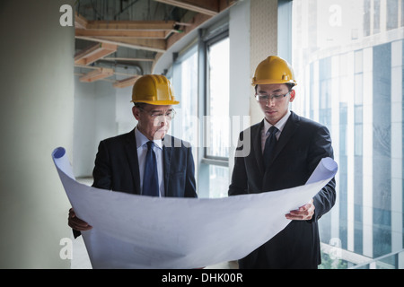 Two architects in hardhats examining a blueprint in an office building Stock Photo