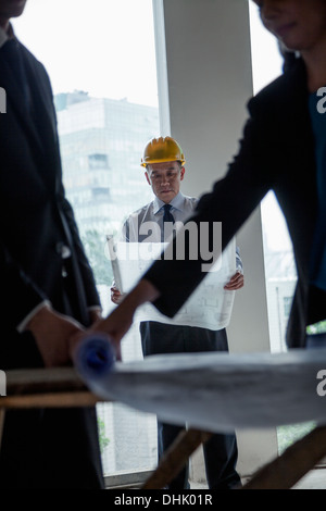 Three architects in hardhats examining blueprints in an office building Stock Photo