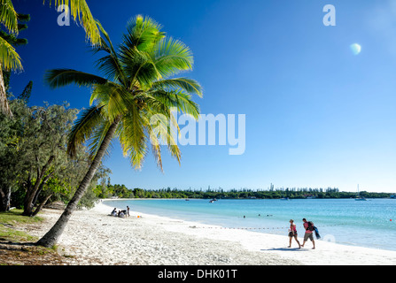People walking on the perfect white sand of a tropical beach, below palm trees and next to the pure blue sea Stock Photo