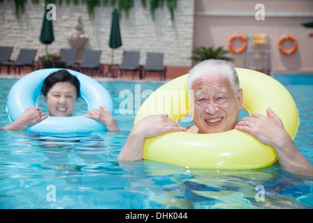 Portrait of senior couple relaxing in the pool with inflatable tubes Stock Photo