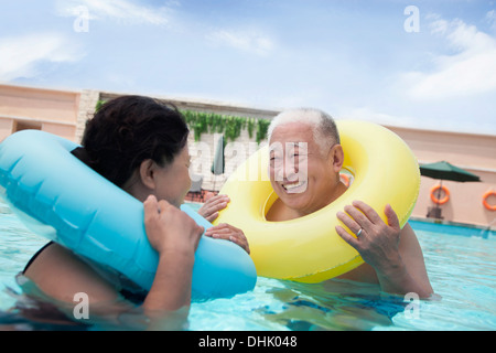 Senior couple smiling and relaxing in the pool with inflatable tubes Stock Photo