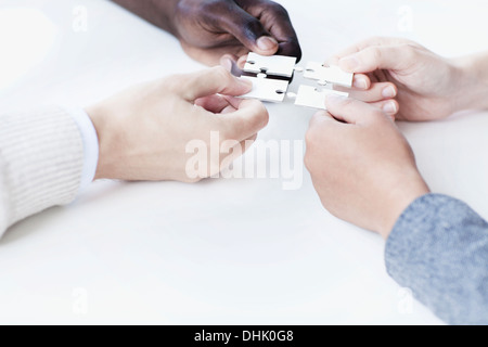 Four business people holding jigsaw puzzle pieces and placing them together, hands only Stock Photo