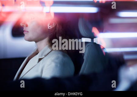 Serene businesswoman sitting in the car at night, illuminated and reflected lights on the car window Stock Photo