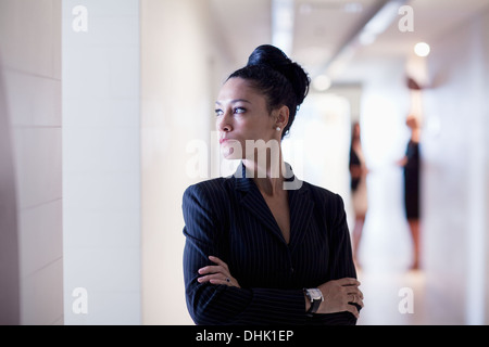 Businesswoman standing in the corridor with arms crossed looking away Stock Photo