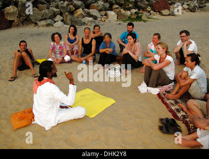 Yoga teacher sitting on the beach talking to his pupils in Varkala,India. Stock Photo