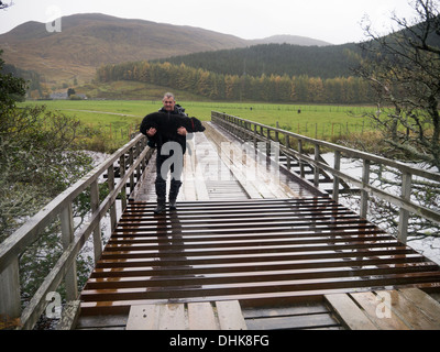 A man carrying a curly coated retriever over a cattle grid on a bridge in Srathconon, Scotland. Stock Photo
