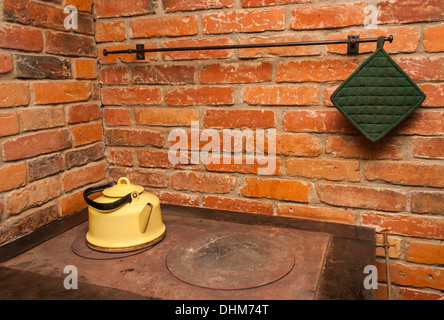 Yellow tea pot on a stove, red brick wall in background Stock Photo