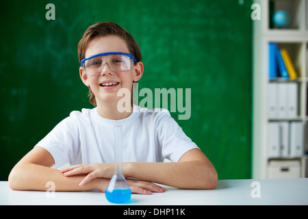 Portrait of smiling schoolboy sitting at workplace with chemical liquid in front Stock Photo