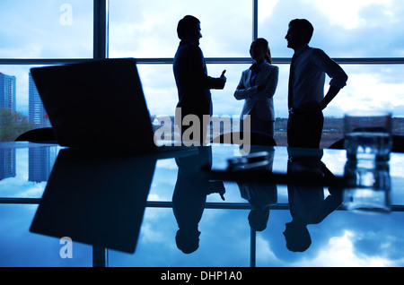 Three office workers interacting by the window with their workplace in front Stock Photo