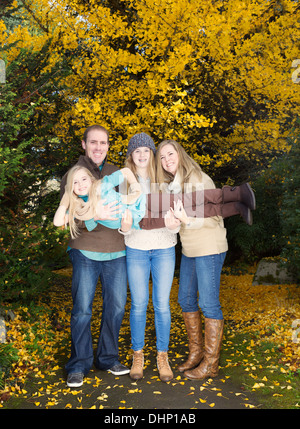 Vertical photo of family holding up their smallest daughter while taking a walk in the park during an autumn day Stock Photo