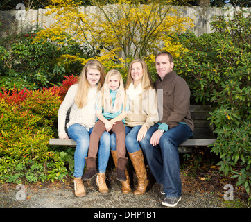 Photo of family all sitting on park bench during a nice day in the fall season Stock Photo