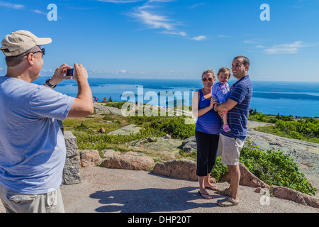 An adult male holds a camera in preparation for photographing a husband, wife and small child in Acadia National Park, Maine. Stock Photo