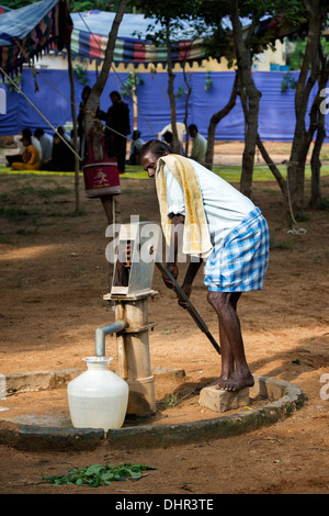 Indian man filling a plastic water pot from a hand pump at the Sathya Sai Baba mobile outreach hospital. Andhra Pradesh, India Stock Photo