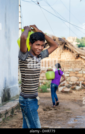 Indian teenage boy carrying a water pot away from a well in a rural Indian village street. Andhra Pradesh, India Stock Photo