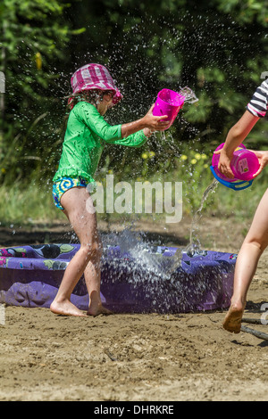 Fun in the sand, at the beach. Cute, model released young girl, having a water fight and getting splashed.