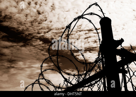 A barbed wire prison fence silhouetted  against a dark, amber moody sky.