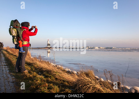 Netherlands, Marken, Ijsselmeer Lake. Winter. Lighthouse called Het Paard. Hiker, woman with child on her back takes picture Stock Photo