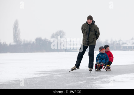 Netherlands, Loosdrecht, Lakes called Loosdrechtse Plassen. Winter. Father ice skating with sons on sledge Stock Photo