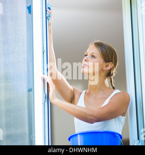 Pretty, young woman doing house work - washing windows (shallow DOF; color toned image) Stock Photo