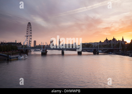 The London Eye, Houses of Parliament and Jubilee Bridge on the River Thames at sunset in London, England Stock Photo